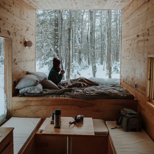 The bed under a full-height window looking into snowy woods