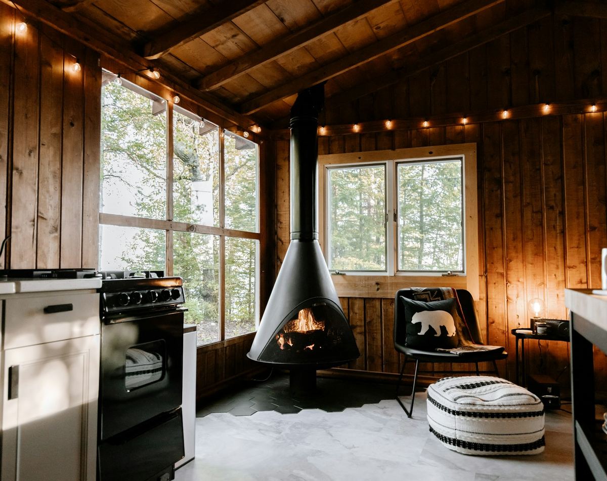 The main room — suspended wood stove, kitchen along the left wall, windows into the oaks