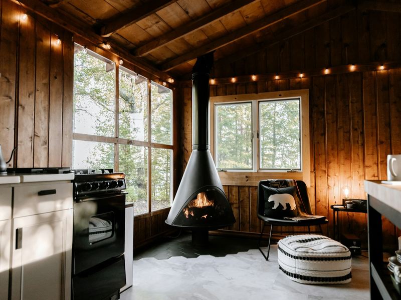 The main room — suspended wood stove, kitchen along the left wall, windows into the oaks