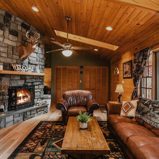 The living room — stone fireplace lit, leather sofas under a vaulted pine ceiling