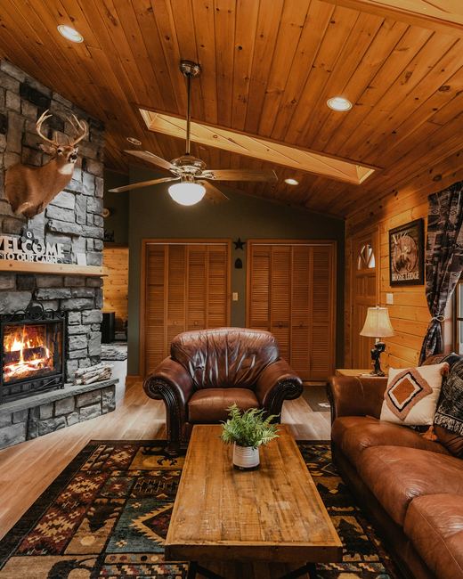 The living room — stone fireplace lit, leather sofas under a vaulted pine ceiling